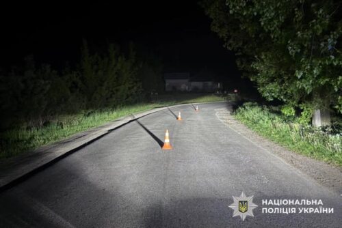 Nighttime street with orange traffic cones guiding traffic; police badge and 'National Police of Ukraine' text visible in the bottom-right corner.