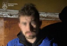 Pixelated man in a blue jacket seated against a wooden wall; Ukrainian Prosecutor's Office watermark in the top-left corner.