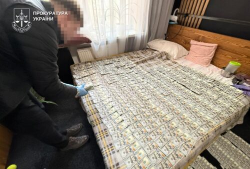 Bedroom scene: bed covered with numerous bundles of cash; investigators in gloves standing beside the bed.