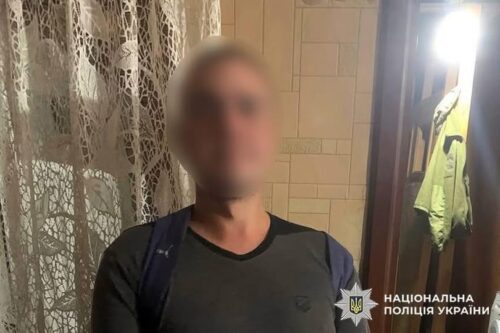 Blurred man standing in a doorway inside a tiled hallway with a backpack; police watermark in the bottom right corner.