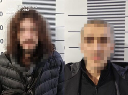 Two blurred adults posing for a police mugshot against a height chart backdrop with measurement lines behind them.