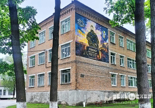 Three-story brick building framed by trees, with a large mural of a soldier on the corner wall.