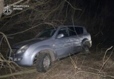 Blue pickup truck entangled in branches in a dark forest at night; Ukraine Prosecutor's Office watermark in the top-left.