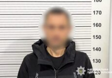 Blurred man in a dark jacket stands against a height chart in a police mugshot setup.