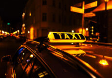 Taxi with illuminated 'TAXI' sign on a dimly lit city street at night.