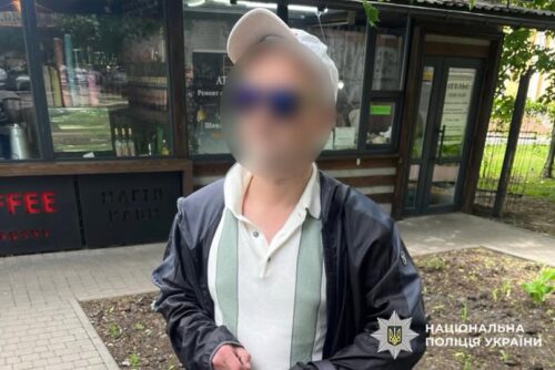 Man wearing a white cap and striped polo shirt, outdoors near a cafe, his face blurred for privacy; police watermark in corner.