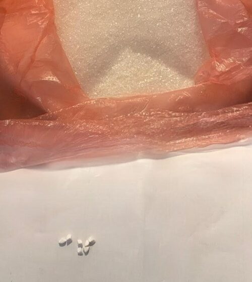 Small white pellets spilled from a pink plastic bag onto a white surface.