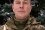 Portrait of a soldier in camouflage and a maroon beret with an emblem, standing in front of trees; memorial banner reads 'ВІЧНА ПАМ’ЯТЬ ГЕРОЮ!' with a lit candle in the foreground.