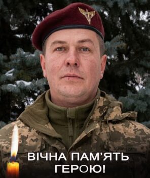 Portrait of a soldier in camouflage and a maroon beret with an emblem, standing in front of trees; memorial banner reads 'ВІЧНА ПАМ’ЯТЬ ГЕРОЮ!' with a lit candle in the foreground.