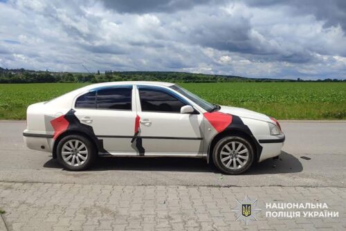 White sedan with red and black graphic artwork on its doors, parked on a rural roadside; Ukrainian police watermark in corner.