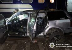 Silver SUV with open doors and visible damage beside a blue train car at night; Ukrainian police watermark