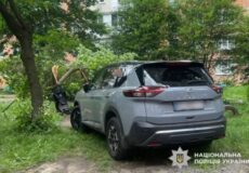 Gray SUV with rear-end damage parked on grassy ground under trees; Ukrainian police watermark in bottom-right corner.