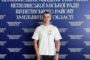Young man in a white T-shirt stands in front of a blue backdrop covered with Ukrainian text the far wall.