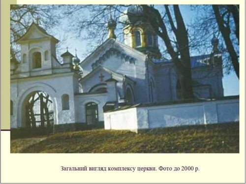 Exterior view of a white Orthodox church complex with arched gateway and surrounding fence, trees in the background.