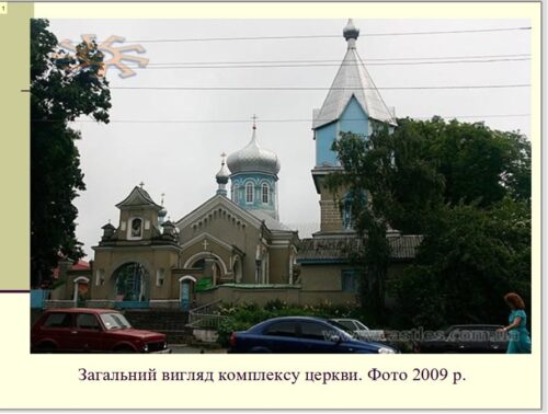 General view of an Orthodox church complex with domed towers, blue accents, and surrounding trees, on a street with cars (photo from 2009).