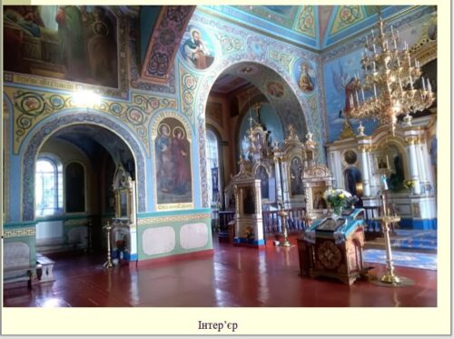 Interior of an ornate Orthodox church with blue walls, arches, icons, and gold chandeliers.