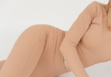 Person wearing a beige bodysuit lying on their side, cropped from shoulders to thighs.