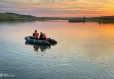 Two people in an inflatable boat paddling on a calm river at sunset the water reflecting the orange sky.