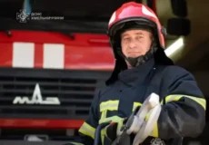 Firefighter in turnout gear and a red helmet stands in front of a red fire truck.
