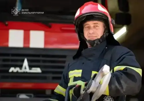 Firefighter in turnout gear and a red helmet stands in front of a red fire truck.