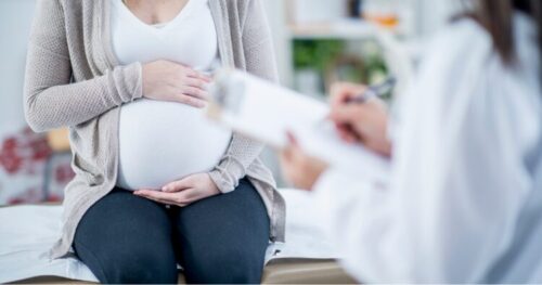 Pregnant woman sitting on an exam table while a clinician shows her a document or form nearby