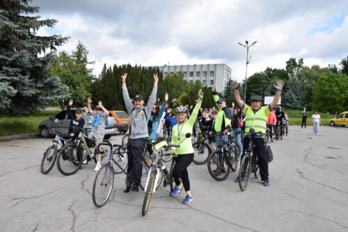 Group of cyclists with helmets raising their hands in a parking lot, posing for a photo during a biking event.