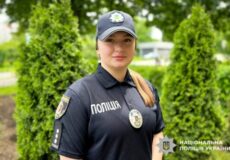Ukrainian police officer in uniform outdoors, wearing cap and badge.