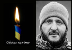 Two-panel memorial: left side shows a lit candle with blue and yellow ribbon and the text 'Вічна пам'ять' on a black background; right side is a grayscale close-up portrait of a bearded man wearing a beanie.