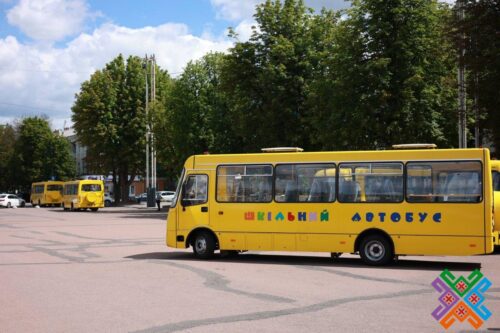 Yellow school buses parked in a lot under a blue sky; a bus displays the Cyrillic text 'ШКОЛЬНЫЙ АВТОБУС'.