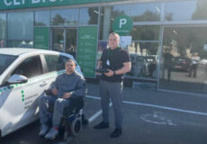 Disabled man in a wheelchair and a staff member stand outside a service center with a parked car; large green Ukrainian 'СЕРВІСНИЙ ЦЕНТР' sign visible.