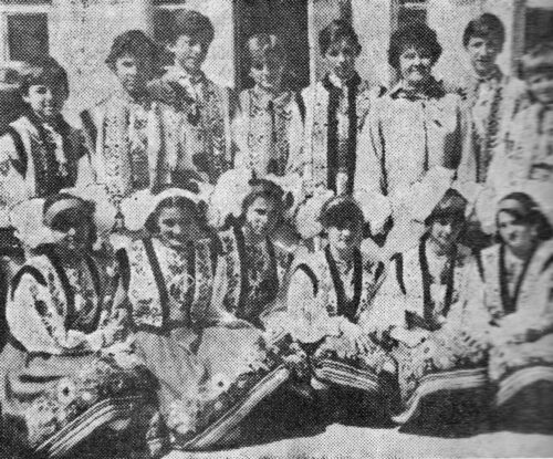 Vintage black-and-white photo of a group of people in traditional folk costumes posing together, some seated with a drum in front.