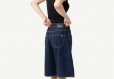 Model wearing a black sleeveless top and knee-length blue denim bermuda shorts, in a side pose with sunglasses; brand tag visible on back waistband.
