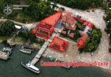 Aerial view of a riverside site with three buildings outlined in red as illegally built structures; watermark of the Ukrainian Prosecutor's Office in the corner.