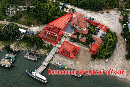Aerial view of a riverside site with three buildings outlined in red as illegally built structures; watermark of the Ukrainian Prosecutor's Office in the corner.