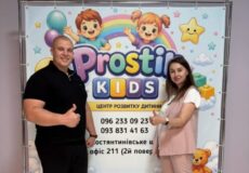 Man and woman pose with thumbs up in front of a colorful 'Pros Kids' banner for a child development center.