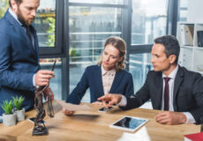 Three professionals in a meeting examining documents on a wooden table in a modern office.