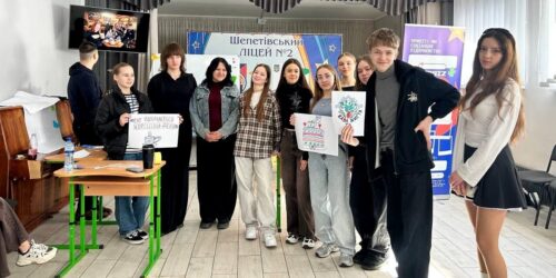 Group of students and mentors posing in a classroom, holding handmade signs for a project or club.