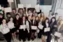 Large group of students in a classroom, smiling and holding certificates toward the camera, as if celebrating a ceremony.