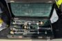 Open hard-shell case with a disassembled clarinet: mouthpiece, barrel, and three instrument sections laid inside with green lining.