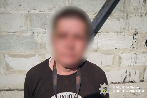 Blurred man in a black shirt wearing a lanyard stands against a concrete wall; Ukraine National Police watermark bottom right.