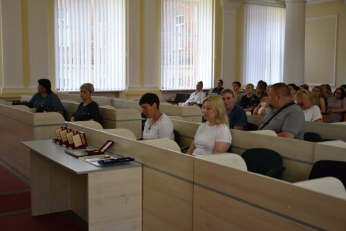 Audience seated in a light-colored conference room, attentively listening to a presentation.