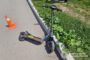 Electric kick scooter tipped over on a paved road beside a curb, with an orange traffic cone nearby and grass along the roadside; Ukrainian police watermark in the corner.