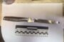 Evidence photo: metal knife with ribbed handle laid on white sheet beside a scale ruler; watermark from Ukrainian Prosecutor's Office in corner.