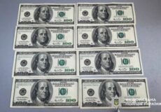 Twelve US $100 bills laid out in two columns on a gray surface, arranged in six rows.