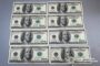 Twelve US $100 bills laid out in two columns on a gray surface, arranged in six rows.