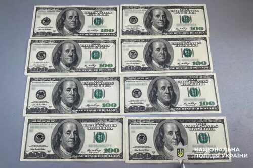 Twelve US $100 bills laid out in two columns on a gray surface, arranged in six rows.