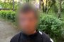 Person with a blurred face standing on a park path, wearing a black Nike jacket and backpack, with a police watermark in the corner.