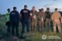 Group of uniformed officers standing in a field with blurred detainees, some in camouflage, in a police operation scene; Ukrainian National Police logo visible on the bottom right.