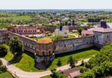 Aerial view of a large medieval castle with crenellated stone walls and towers set in green farmland.