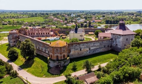 Aerial view of a large medieval castle with crenellated stone walls and towers set in green farmland.